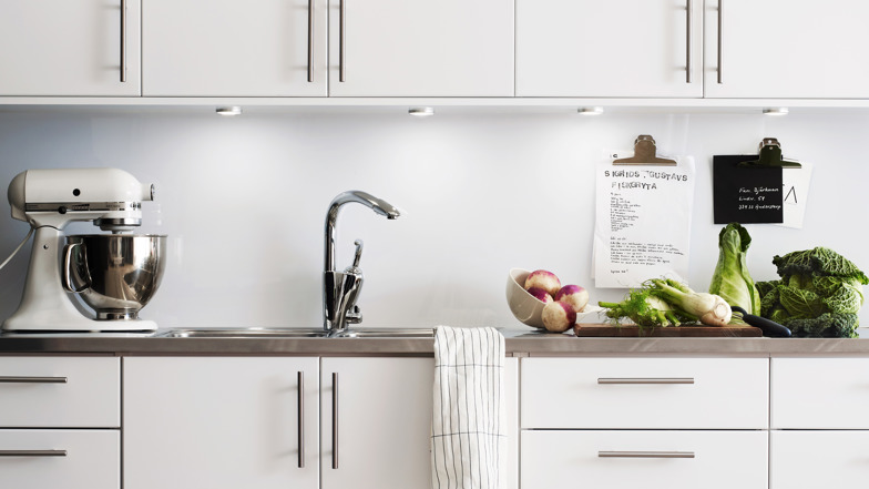 Närbild på ett vitt kök med en bänk med grönsaker på. 