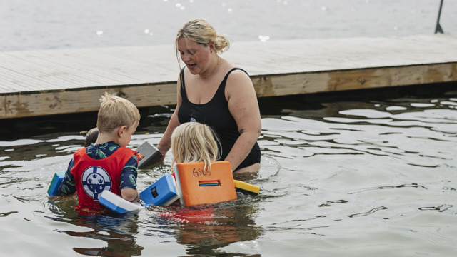 En simskolelärare håller yngre barn i handen och bildar en ring för att träna vattensäkerhet i simskolan vid Sisjön i Mölndal. 
