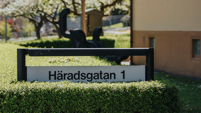 Vårlig vy med skylt där det står Häradsgatan 1 och en bit av Mölndalsbostäders kontor i bakgrunden. 