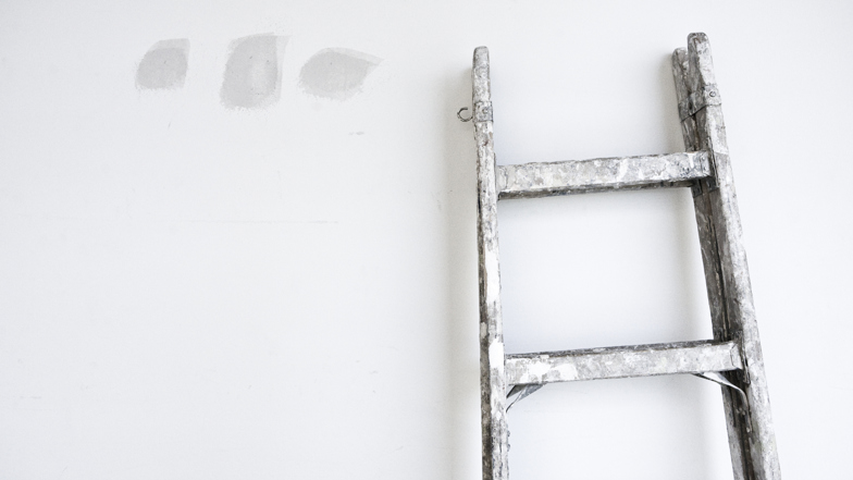 En vägg med spackel och en stege lutad mot.