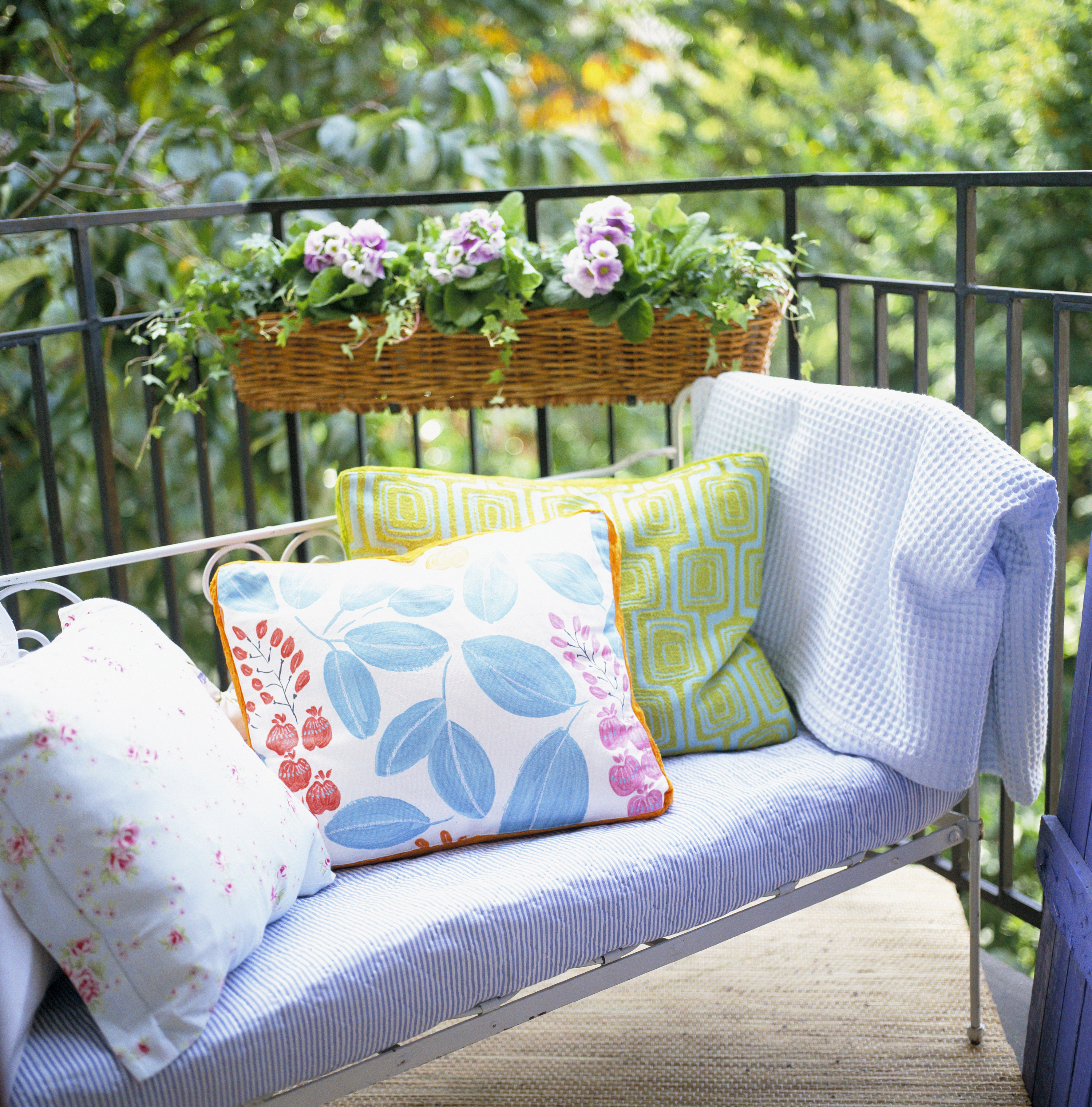 En soffa med kuddar och mjukpläd på en balkong med en blomsterlåda på insidan av räcket. 