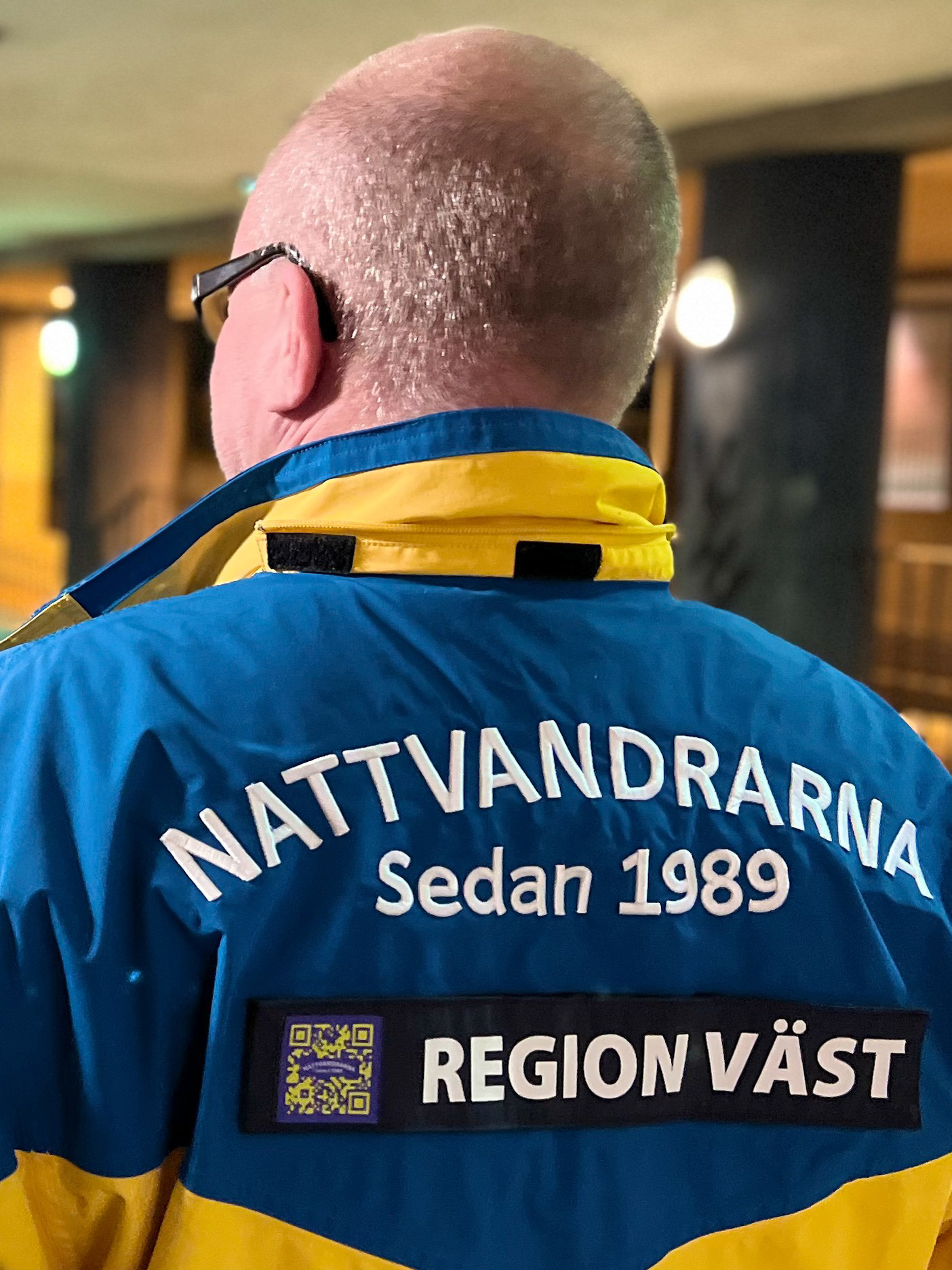 En man i närbild bakifrån med en jacka där texten Nattvandrarna Region Väst är i fokus. 