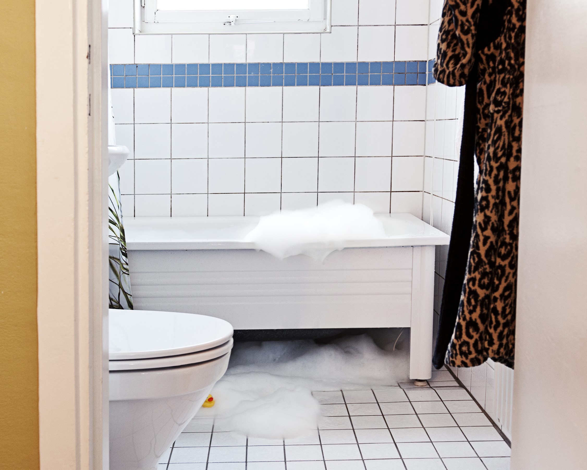 Ett badrum med badkar där skummet har runnit över och ut på golvet.