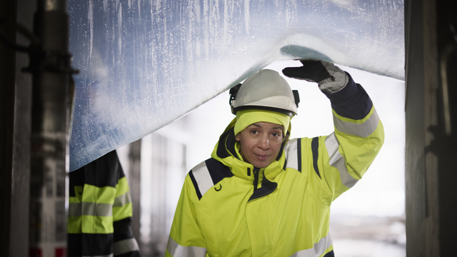 Kvinna med bygghjälm med en byggställning i bakgrunden. 