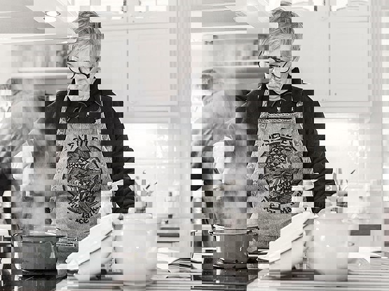 Äldre kvinna lagar mat vid spisen och rör om i en gryta.